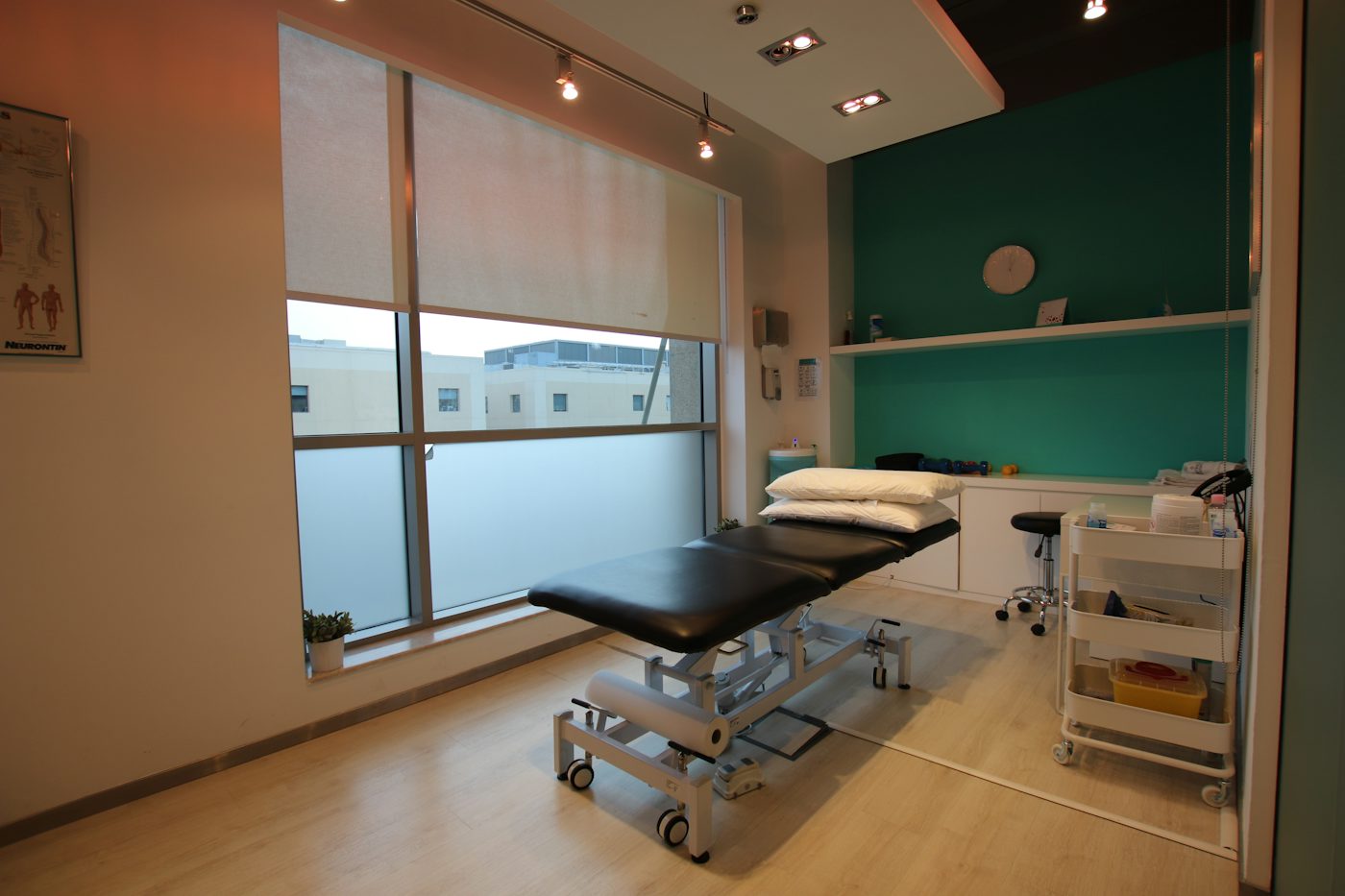 A bright treatment room with a padded couch beside a tall window