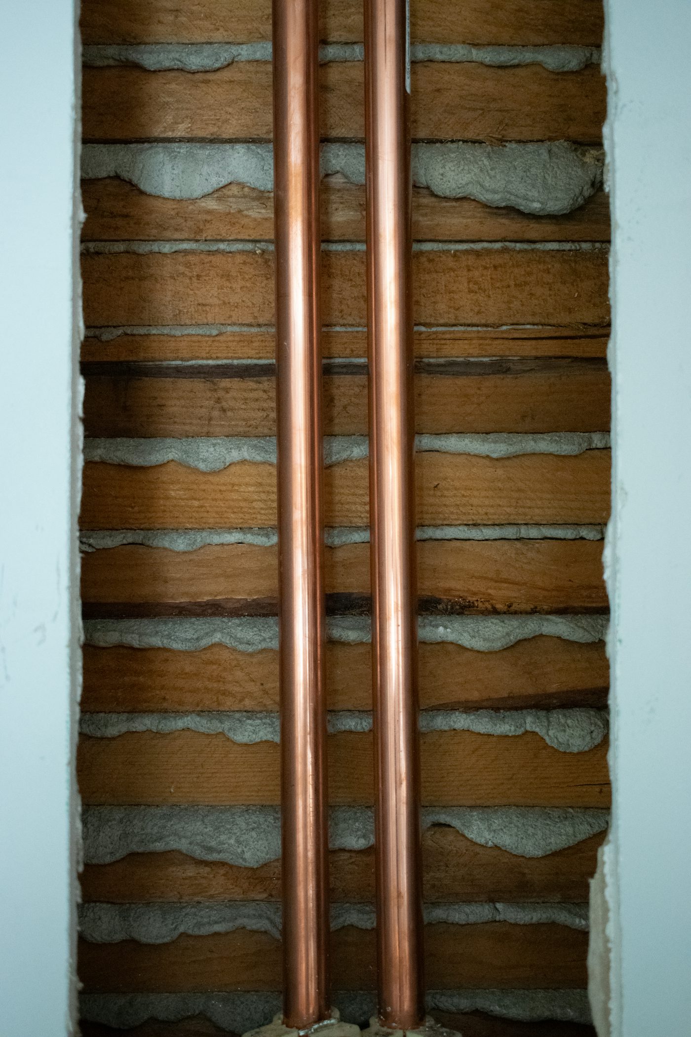 Two copper pipes running up a painted brick wall